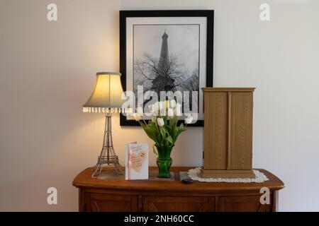 Muttertagsgeschenk mit weißen und gelben Tulpen und eine Karte sind in meinem Wohnzimmer auf einem Tisch ausgestellt. Der Fotodruck auf dem Eiffelturm ist meine eigene Arbeit. Stockfoto