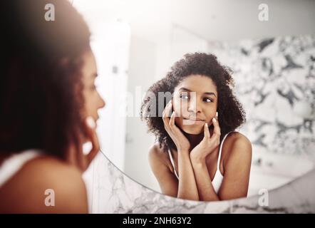 Ich fühle mich fabelhaft und sehe fabelhaft aus. Eine attraktive junge Frau, die ihr Gesicht im Badezimmerspiegel bewundert. Stockfoto