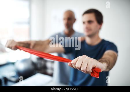 Pass auf, dass du dich nicht verletzt. Ein Physiotherapeut, der einem Patienten mit Widerstandsbändern hilft. Stockfoto