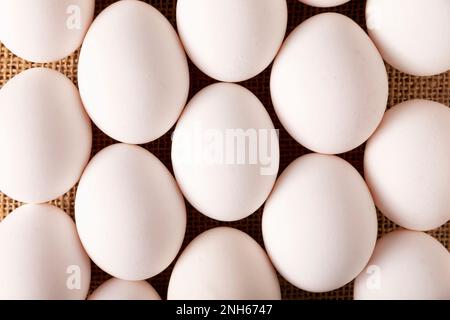 Weiße Hühnereier auf Leinenstruktur. Sehr beliebtes nahrhaftes und wirtschaftliches Lebensmittelprodukt. Obere Tabellenansicht. Stockfoto