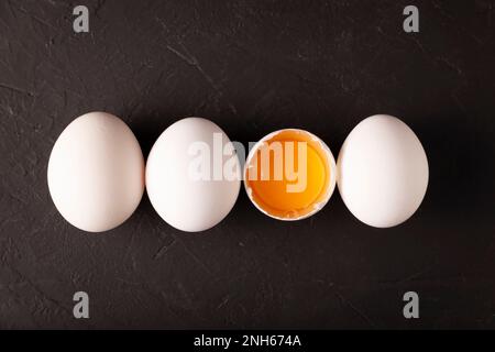 Weiße Hühnereier und Eigelb in einer Reihe auf schwarzer Konsistenz. Sehr beliebtes nahrhaftes und wirtschaftliches Lebensmittelprodukt. Konzeptbild. Obere Tabellenansicht. Stockfoto