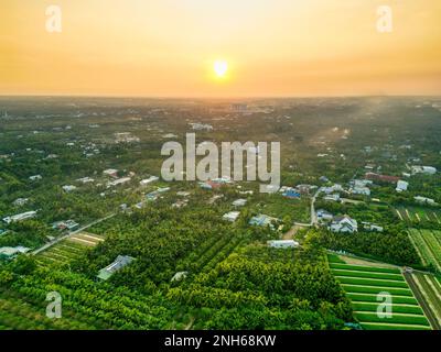 Golden Hour Magic: Atemberaubender Sonnenuntergang über den Feldern der Provinz Tien Giang mit dem ruhigen Fluss und der Stadtlandschaft in Vietnam Stockfoto