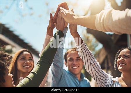 Auf einen tollen Tag vor uns. Eine Gruppe fröhlicher junger Freunde, die sich zusammendrängen und sich tagsüber draußen ein paar High Five geben. Stockfoto