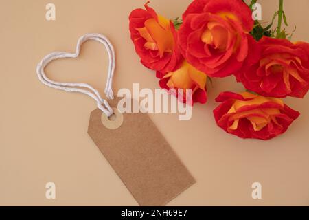 Einfarbige beige Papiernote und Seil in Herzform auf neutralem beigen Hintergrund. Zarte rote Rosen Grußkarte Feiertagsidee. Erstellen Sie einen Kopierplatz für Text. Geschenk Stockfoto