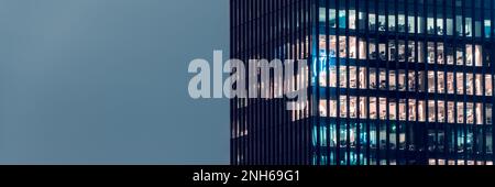 Nahaufnahme eines Bürogebäudes am Abend mit einigen beleuchteten Arbeitsbereichen vor dem Nachthimmel mit Dartpfeilen. Moderner, verglaster Wolkenkratzer. Finanzdistrikt. La Stockfoto