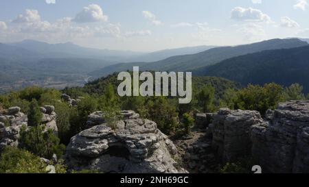 Blick von oben auf wunderschöne graue Felsformationen zwischen grünen Bäumen. Panoramablick aus der Vogelperspektive auf die Berge und den Himmel an einem Sommertag. Stockfoto