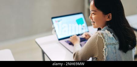 Glückliches asiatisches Mädchen, das Code auf einem Laptop lernt. Sie sitzt in einem Klassenzimmer für Computerkenntnisse, nimmt an der Lektion Teil und nimmt an einer Programmierung Teil Stockfoto