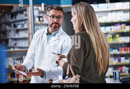 Abgabe von Arzneimitteln und Beratung. Ein reifer Apotheker, der einer jungen Frau in einer Apotheke assistiert. Stockfoto