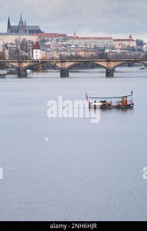 Blick auf die Stadt am Vormittag entlang der Moldau mit einer Fähre, Schwanen, Brücke und der Prager Burg St. Veitsdom im Hintergrund Stockfoto