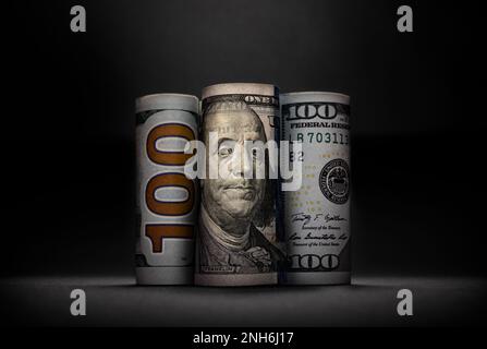 Drei verschiedene Bilder von 100 US-Dollar in Rollen auf dunklem Hintergrund Stockfoto