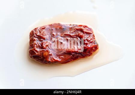 Nahaufnahme eines Stücks getrockneter oder sonnengetrockneter roter Tomaten mit Öl auf weißer Keramikplatte Stockfoto