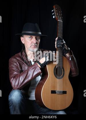 Ein Mann mit Hut und Gitarre auf schwarzem Hintergrund. Selbstporträt. Stockfoto