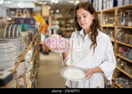 Frau wählt Teller im Geschirrladen Stockfoto