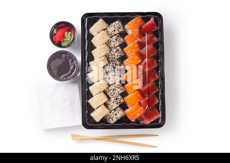 Sushi-Set mit Wasabi, Ingwer und Sojasoße, serviert in einer Plastikbox zum Mitnehmen. Gemischtes japanisches Sushi mit Thunfisch, Lachs, Sesam isoliert auf WH Stockfoto