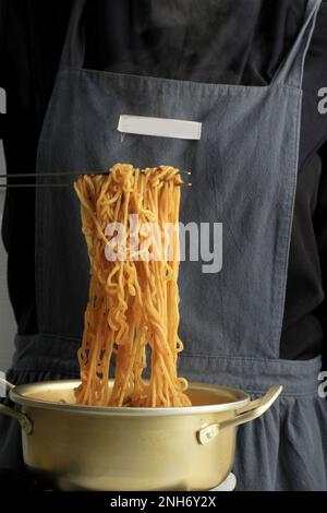Frau, die eine Edelstahlzange zum Kochen von Ramyeon oder koreanischer Instant Noodles Suppe in einem Koreanisch gelben Aluminiumtopf auf einem Gasherd verwendet Stockfoto