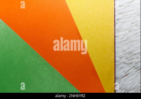 Ein Bündel hochwertiges farbiges Papier liegt auf weißem Hintergrund. Dreifarbige geometrische Oberfläche, Orange, Gelb und Grün Stockfoto