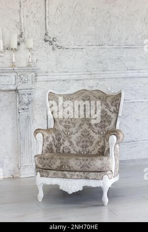 Neben einem dekorativen Kamin und Kerzen befindet sich ein schöner neuer Sessel im klassischen Stil in einem Saal mit stilvoller Innenausstattung Stockfoto