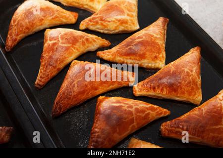 Frisch gebackene, köstliche, heiße Brötchen, gefüllt mit Ofen, dreieckige Form liegen auf einem Backblech Stockfoto