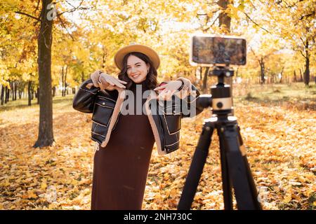Stylen Sie eine Frau, die ein Smartphone mit Stabilisator verwendet, und im Herbstpark Fotos und Live-Videos macht. Vlog, Video-Blogging, Outdoor-Fotografie-Konzept. C Stockfoto