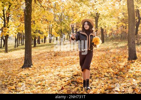 Modernes Smartphone-Gerät auf Stativ Aufnahme junge weibliche Sprecherin, die im Herbst live aus dem Park im Internet überträgt, Handy-Gerät Shoot Woman BL Stockfoto