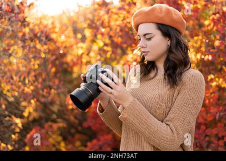 Eine junge Fotografin mit der Kamera, die Fotos vom Herbstpark mit gelbem Wald macht. Eine Dame, die im Herbstpark mit gelben und orangefarbenen Blättern spaziert. Stockfoto