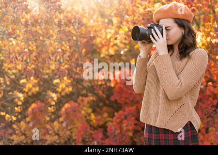 Eine wunderschöne junge Frau macht Fotos mit der Kamera in einem Wald, der das Herbstwetter genießt. Ruhe, Entspannung, Lifestyle-Konzept. Stockfoto