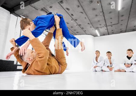 Lehrer, Profi-Judo, Jiu Jitsu-Trainer-Trainingstypen, Jungs, zeigen Übungen. Kinder lernen drinnen Stockfoto