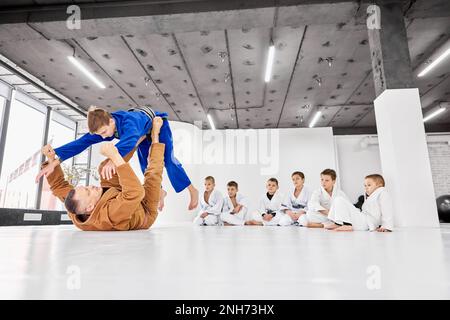 Professionelles Judo, Jiu-Jitsu-Trainer, der Sport macht, drinnen trainiert. Kinder schauen aufmerksam auf den Trainer Stockfoto