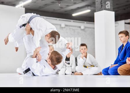 Dynamisches Porträt. Jungs, Kinder im weißen Kimono-Training, Judo-Übungen, Jiu-Jitsu-Übungen drinnen. Achtung Stockfoto