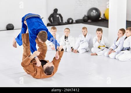 Lehrer, Profi-Judo, Jiu Jitsu-Trainer-Trainingstypen, Jungs, zeigen Übungen. Kinder schauen aufmerksam zu Stockfoto