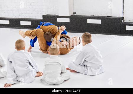 Lehrer, Profi-Judo, Jiu Jitsu-Trainer-Trainingstypen, Jungs, zeigen Übungen. Kinder lernen drinnen. Aufmerksame Kinder Stockfoto