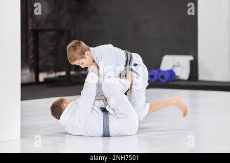 Jungs, Kinder im weißen Kimono-Training, Judo-Übungen, Jiu-Jitsu-Übungen drinnen. Wachsende Stärke, sportliche Kowledges Stockfoto