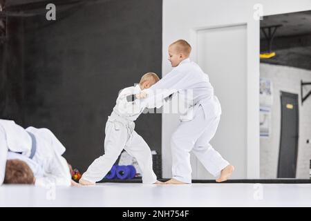 Verteidigung. Jungs, Kinder im weißen Kimono-Training, Judo-Übungen, Jiu-Jitsu-Übungen drinnen. Profisportler Stockfoto