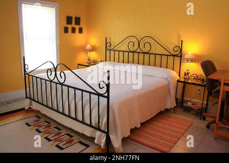 Goldenes Schlafzimmer im Montebello Bed and Breakfast Inn mit einem schmiedeeisernen Bett und mexikanischen Teppichen auf dem Boden. Stockfoto