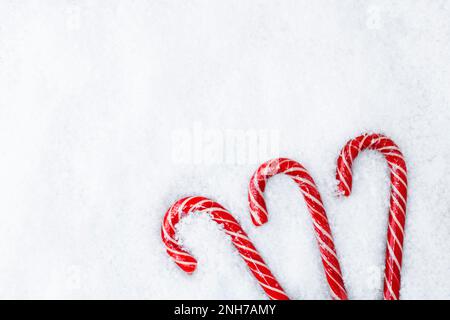 Komposition von drei weihnachtlichen Zuckerstangen auf weißem verschneitem Hintergrund. Draufsicht. Platz für Text. Stockfoto