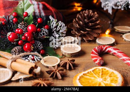 Hintergrundbanner für Weihnachtsgrüße und Neujahr. Weihnachtszweig auf einem hölzernen Hintergrund neben Orangen, würzigen Gewürzen und einem gefrorenen Stock. Stockfoto