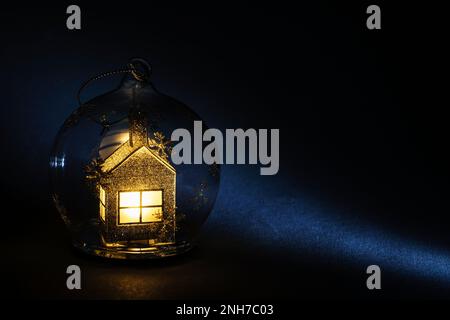 Transparenter Weihnachtsball mit einem glänzenden, goldfarbenen Hausgebäude innen auf dunkelblauem Hintergrund. Postkartenbanner für Weihnachten und Neuheiten Stockfoto