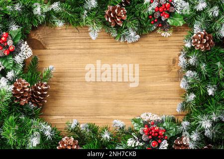 Weihnachtsgrenze bestehend aus schneebedeckten Tannenästen und -Zapfen auf weihnachtlichem Holzhintergrund. Hintergrund für Winterferien. Draufsicht. Flach. Kopie sp Stockfoto