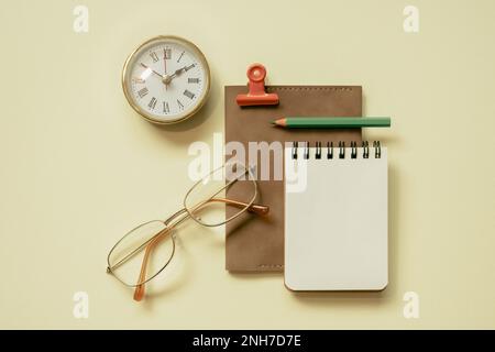 Notizblock, Tagebuch, Uhr, Brille, Stift, Gelber Schreibtischhintergrund mit Clipbefestigung. Flay-Lay, Draufsicht, Kopierbereich Stockfoto