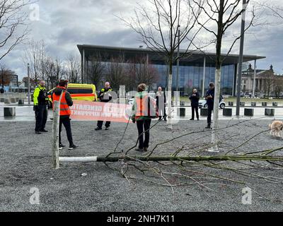 21. Februar 2023, Berlin: Klimaschutzdemokraten stehen mit dem Rücken zum Bundeskanzleramt vor einem gefällten Baum. Klimaschutzdemokraten haben am Dienstagmorgen vor dem Kanzleramt in Berlin einen kleineren Baum gefällt. Die Polizei war wegen der Aktivisten im Regierungsgebäude im Dienst, sagte ein Sprecher. Die Last Generation Protest Group schrieb auf Twitter über die Aktion: „Wirtschaft und Politik sägen sich an den Zweigen, auf denen die Zivilisation sitzt. Wir machen diese Zerstörung mitten in Berlin sichtbar." Foto: Julius-Christian Schreiner/TNN/dpa Stockfoto