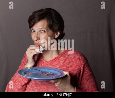 Ältere Frau mit leerem blauem Teller Stockfoto