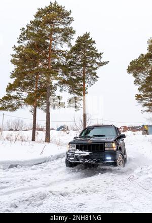 Geländewagen „Jeep Grand Cherokee“ 4x4 mit Geländetraining im Winter auf Schnee im Wald zwischen Kiefern mit einer weiblichen Fahrerin. Stockfoto