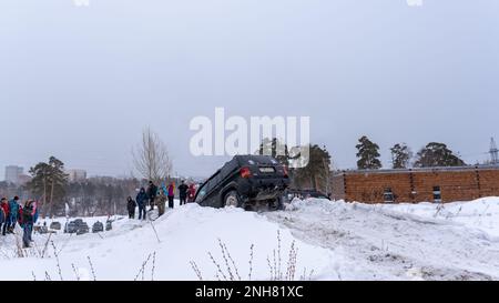 Offroad-SUV „Jeep Grand Cherokee“ in schwarzer Geländewagen-Farbe fällt im Winter von einem steilen Hügel im Schnee ab. Stockfoto