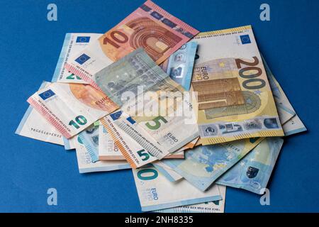 Auf dem Tisch liegt ein Stapel Banknoten in Stückelungen von fünf, zehn, zwanzig, fünfzig und zweihundert Euro. Gemischte Euro-Banknoten auf blauem Hintergrund. Stockfoto