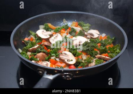 Grünkohl, Pilze, Zwiebeln und rote Paprika, die in einer Pfanne in einem Konvektionsofen gebraten werden Stockfoto