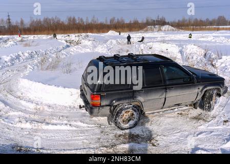 Offroad-SUV „Jeep Grand Cherokee“, schwarz, fährt schnell auf einer scharfen Kurve der Winterstraße im Schnee Stockfoto