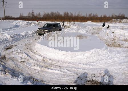 Offroad-SUV „Nissan Patrol 4x4“ fährt im Winter schnell auf dem Schneefeld mit einem lächelnden, fröhlichen Passagier. Stockfoto