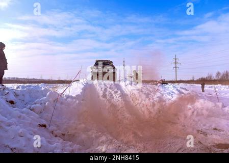 Offroad-SUV „Suzuki Escudo“ fährt im Geländewagen auf einem schneebedeckten Berg in den Wolken des farbigen braunen Rauchs im Winter auf einer kaputten Straße während des Tages. Stockfoto