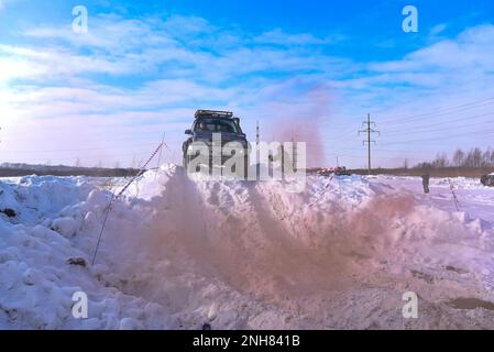 Offroad-SUV „Suzuki Escudo“ fährt im Geländewagen auf einem schneebedeckten Berg in den Wolken des farbigen braunen Rauchs im Winter auf einer kaputten Straße während des Tages. Stockfoto