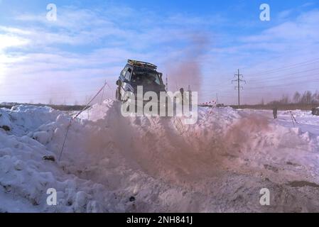 Offroad-SUV „Suzuki Escudo“ fährt im Geländewagen auf einem schneebedeckten Berg in den Wolken des farbigen braunen Rauchs im Winter auf einer kaputten Straße während des Tages. Stockfoto